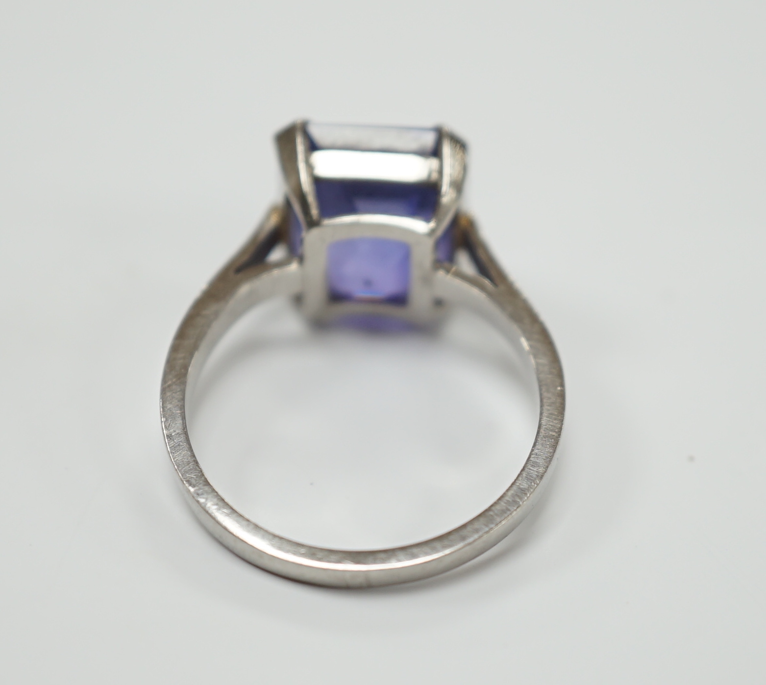 A white metal and single stone and square cut blueish purple sapphire set dress ring, size M, gross weight 5.6 grams, the stone measuring 10mm by 9,8mm, with a depth of 7.4mm.